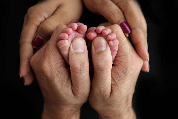 新生儿在父母手中的脚。幸福家庭理念。妈妈和爸爸抱着孩子的腿。工作室摄影在黑色背景的一个孩子的脚趾，脚跟和脚。图片下载