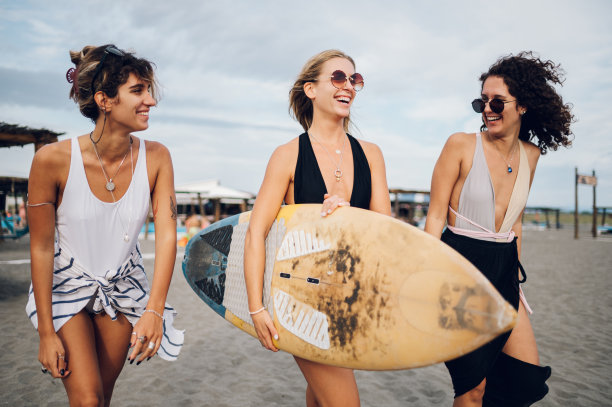 三个迷人的女性朋友在海滩上带着冲浪板散步图片下载