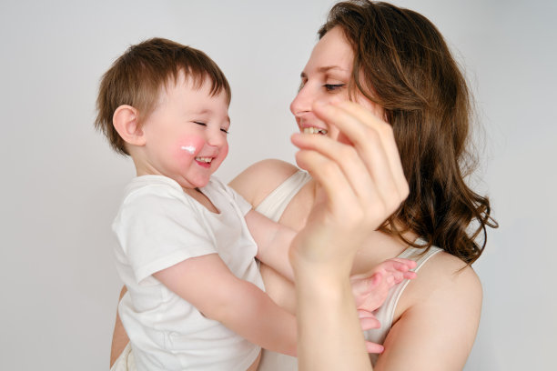 一位母亲在工作室的白色背景上用婴儿面霜涂抹脸颊。妈妈在孩子的脸上涂抹湿疹润肤霜。2岁左右(1岁9个月)图片下载