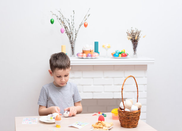 小男孩装饰和画复活节彩蛋对着分散的壁炉上的复活节装饰。有选择性的重点。复活节快乐的概念。在家手工制作的过程图片下载