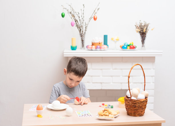 一个小男孩在壁炉上画复活节彩蛋，壁炉上有复活节装饰。有选择性的重点。复活节快乐的概念。在家手工制作的过程图片下载