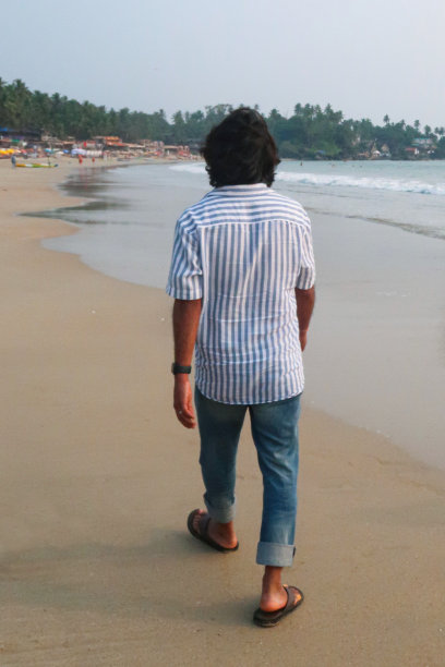 印度果阿，帕洛莱姆，果阿海滩度假的印度人，沿着海水边缘潮湿的沙滩散步，度假游客穿着人字拖在海滩上散步，后视图，焦点在前景图片下载