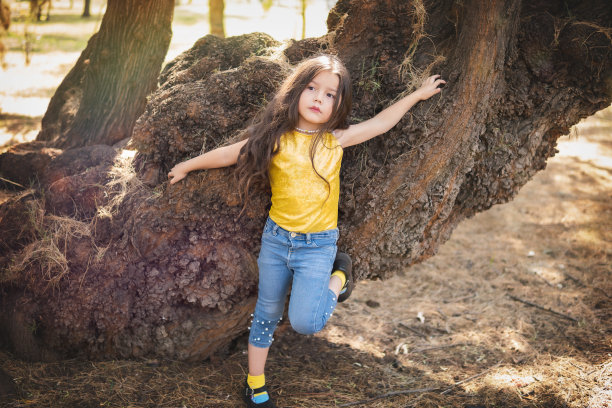 幼儿园小女孩在森林里的一棵树上摆姿势，儿童节的主题。图片下载