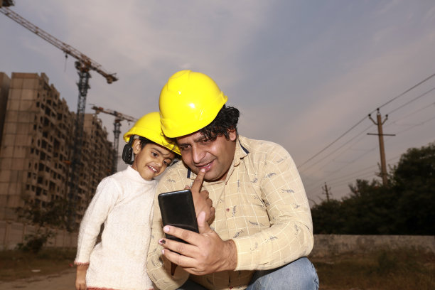 父亲和女儿戴着安全帽在工地附近使用手机图片下载