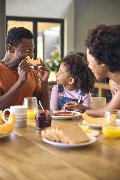父母和女儿在家里吃早餐前用西瓜做鬼脸的家庭照片图片下载