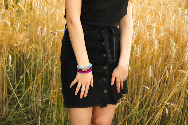 夏天背景下穿裙子的女孩。开朗的年轻女子，有着性感的双腿和黄色小麦背景上的黑色裙子。手戴手镯图片下载