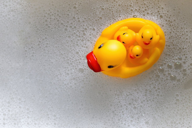 一只橡皮鸭带着三只小鸭子在泡沫中游泳。从高处俯瞰图片下载