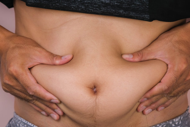 胖男人的手握着多余的腹部脂肪，孤立在粉红色的背景上。男人抚摸着他的大肚子。肥胖的大肚子年轻人图片下载