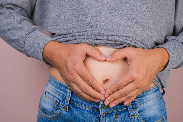 胖女人的手拿着多余的腹部脂肪孤立在粉红色的背景。肥胖的女人的腹部。女性饮食养生理念图片下载