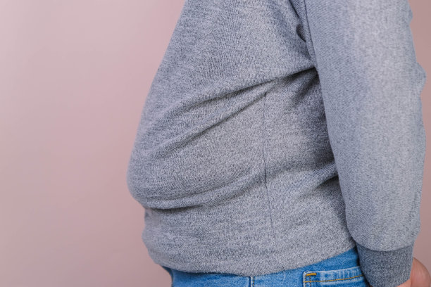 胖女人的手拿着多余的腹部脂肪孤立在粉红色的背景。肥胖的女人的腹部。女性饮食养生理念图片下载