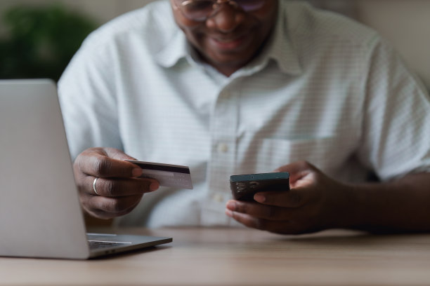 年轻的非洲裔美国人使用手机持有信用卡。银行应用，网上购物概念图片下载