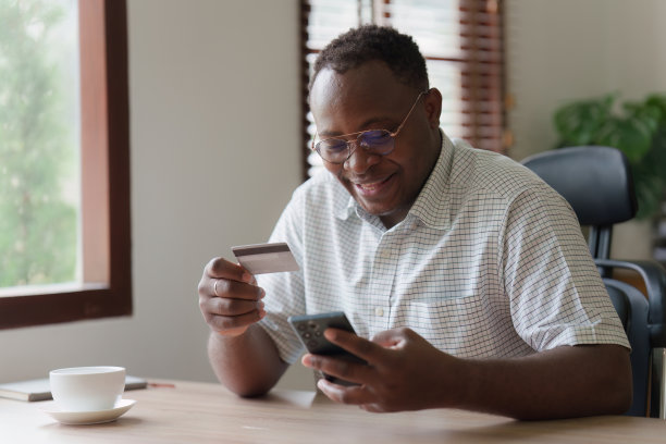 年轻的非洲裔美国人使用手机持有信用卡。银行应用，网上购物概念图片下载