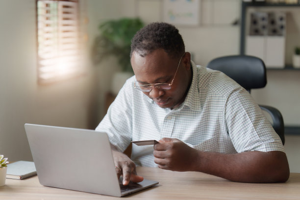 年轻的非洲裔美国人用手提电脑和信用卡。银行应用，网上购物概念图片下载