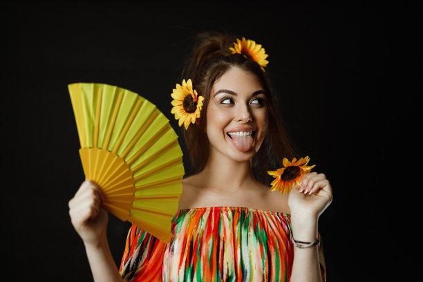 微笑着的年轻女子，头发上插着向日葵，手里拿着一把黄色的扇子图片下载