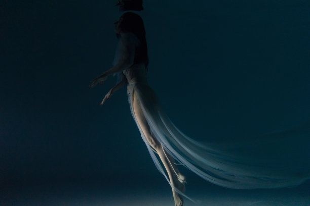 水下拍摄美丽的女人在白色飞行透明的衣服在水中游泳通过阳光。图片下载