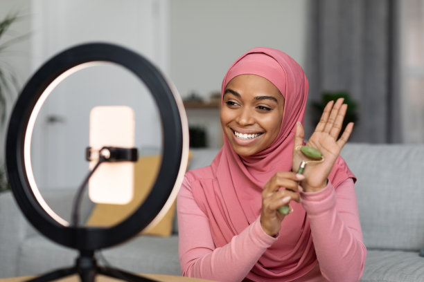 快乐的黑人穆斯林博主女士正在评论滚石机，并在环灯上的智能手机上拍摄视频图片下载