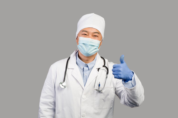 微笑的中年中国男性治疗师，穿着白大褂，戴着防护口罩，听诊器竖起大拇指图片下载