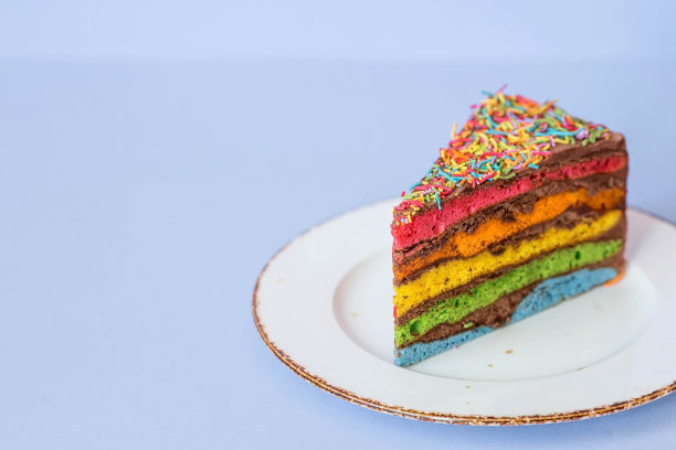 用节日蜡烛和五彩纸屑装饰的彩虹生日蛋糕。糖果。五彩缤纷的甜点，在蓝色的背景上，彩虹的颜色。图片下载