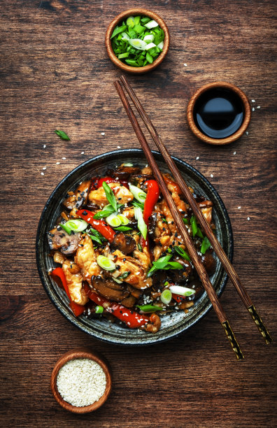 用陶瓷碗将鸡肉与辣椒粉、香菇、香葱和芝麻一起翻炒。亚洲菜。木制厨房餐桌背景，俯视图图片下载