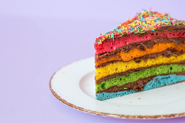 用节日蜡烛和五彩纸屑装饰的彩虹生日蛋糕。糖果。五彩缤纷的甜点，在紫色的背景上有彩虹的颜色。图片下载