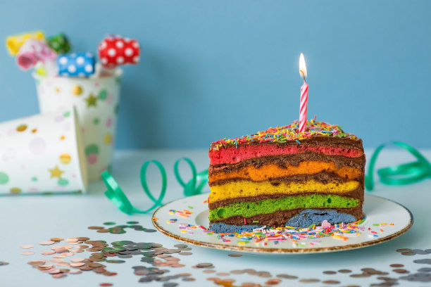用节日蜡烛和五彩纸屑装饰的彩虹生日蛋糕。糖果。五彩缤纷的甜点，在蓝色的背景上，彩虹的颜色。图片下载