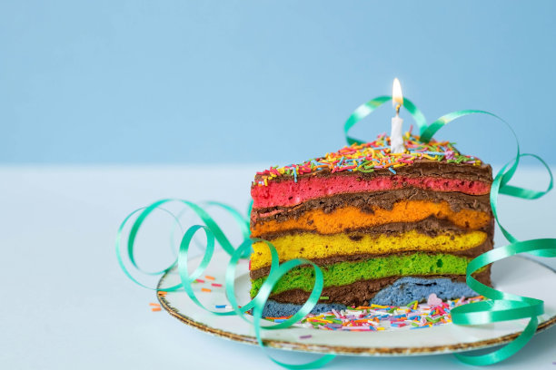 用节日蜡烛和五彩纸屑装饰的彩虹生日蛋糕。糖果。五彩缤纷的甜点，在蓝色的背景上，彩虹的颜色。图片下载