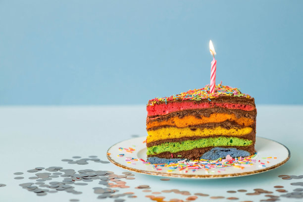 用节日蜡烛和五彩纸屑装饰的彩虹生日蛋糕。糖果。五彩缤纷的甜点，在蓝色的背景上，彩虹的颜色。图片下载