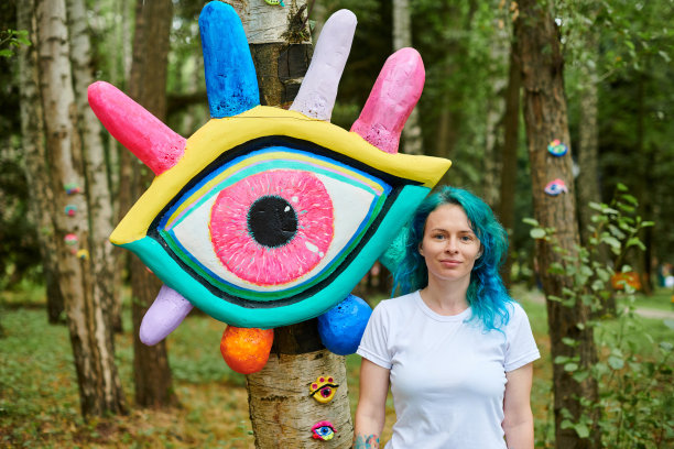 在大眼艺术装置旁，穿着白色T恤，染成蓝绿色头发的微笑年轻成年女子图片下载