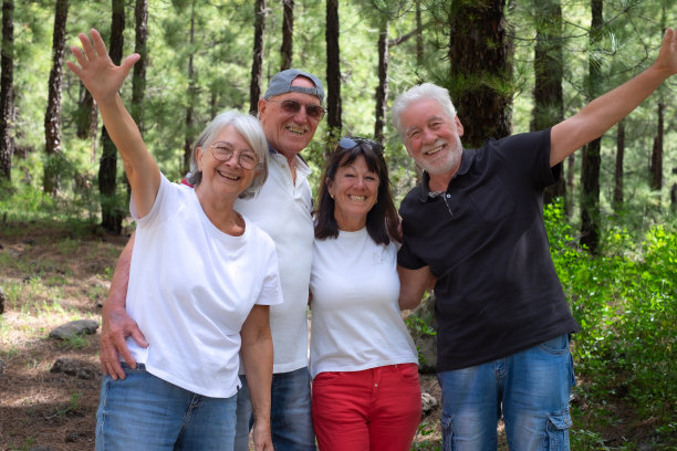 四个快乐的老人站在公园里，张开双臂看着镜头——一群微笑的退休人员一起享受大自然和徒步旅行的日子图片下载