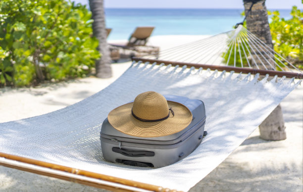 一个手提箱和一顶草帽躺在吊床上，背景是马尔代夫的风景。旅游和热带度假的概念图片下载