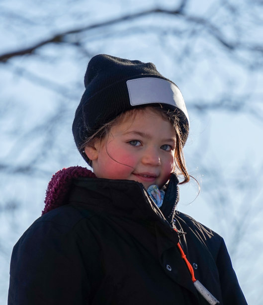 穿着保暖衣服的微笑女孩站在光秃秃的树前的肖像图片下载