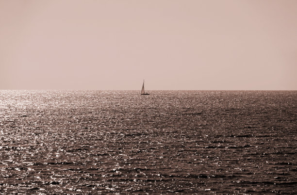 深褐色色调的照片，大海的地平线和帆船在远处图片下载