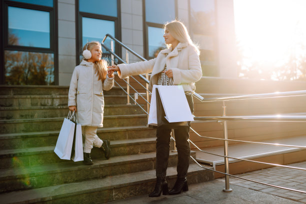 时尚的妈妈和带着购物袋的小女孩在商场附近。图片下载