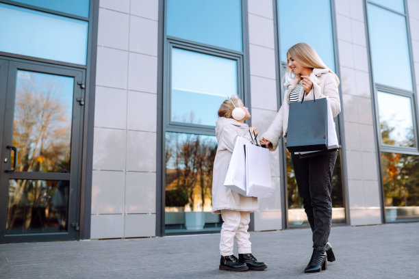 时尚的妈妈和带着购物袋的小女孩在商场附近。图片下载