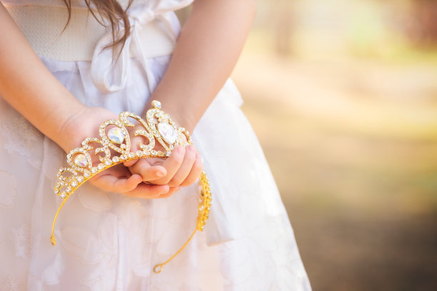 身穿白色连衣裙的小女孩正背着一顶公主王冠，复制空间，儿童节主题图片下载