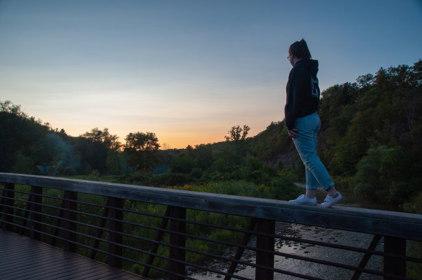 日落时分，一个女人走在山谷森林里的桥栏杆上图片下载
