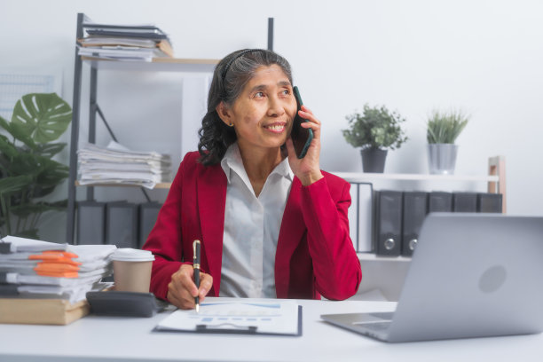 自信的亚洲老年商人，穿着红色套装，坐在办公桌前计划记账项目，思考和阅读，坐在工作场所。图片下载