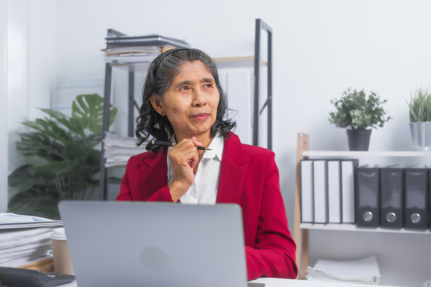 自信的亚洲老年商人，穿着红色套装，坐在办公桌前计划记账项目，思考和阅读，坐在工作场所。图片下载