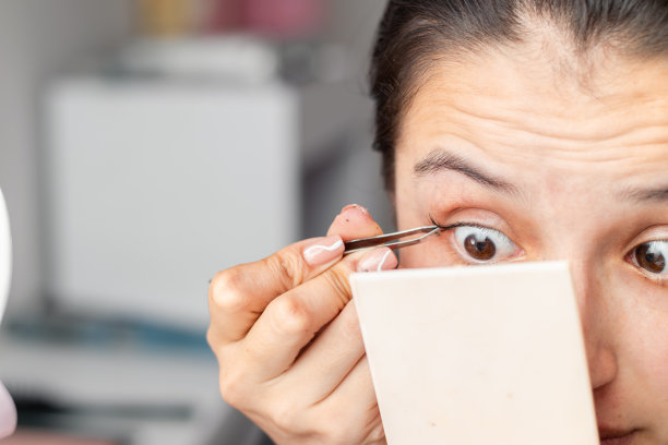 一个拉丁裔妇女用手动眉毛镊子涂假睫毛的详细照片图片下载