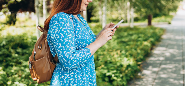 美丽时尚的女人走在城市在夏天的一天，拿着智能手机。电话沟通。城市生活方式概念。查看社交网络，发短信。图片下载