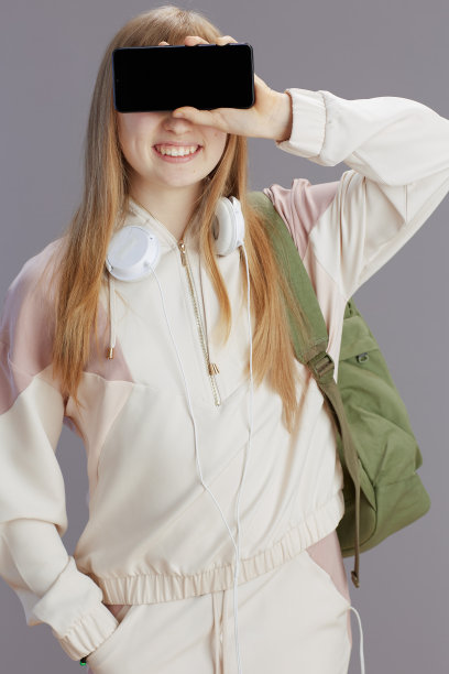 穿着米色运动服的快乐女孩展示着智能手机的空白屏幕图片下载