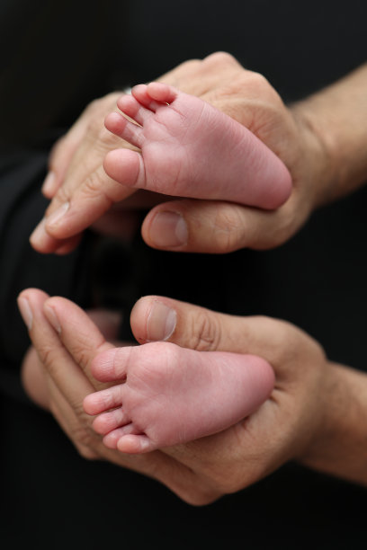 一位母亲用黑色背景的黑色毯子抱着新生儿的脚。新生儿的脚握在父母手中。工作室微距照片腿，脚趾，脚和脚跟的新生儿。图片下载