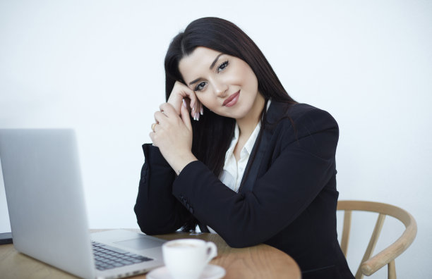 女商人一边用笔记本电脑工作，一边对着镜头微笑。图片下载