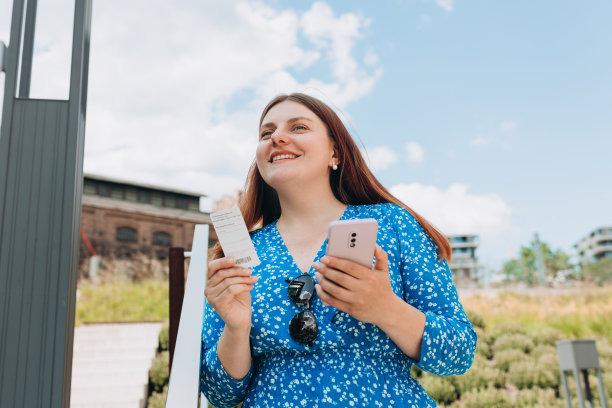 非常快乐的红发女人站在城市背景上，手里拿着车票和手机。公交或地铁车票在女人手上图片下载