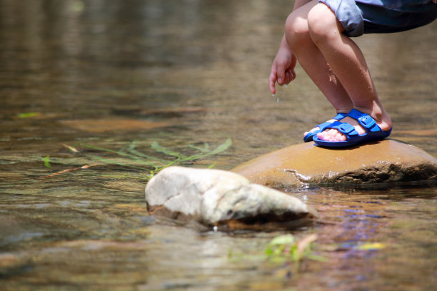 亚洲男婴穿着拖鞋站在小溪里的一块石头上图片下载