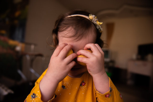 穿着礼服的小女孩在脸附近拿着两个用天然姜黄颜料涂成的复活节彩蛋。肖像图片下载