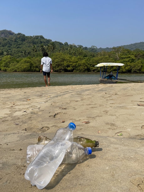 特写照片:退潮时被冲到沙滩上的三堆塑料水瓶，海岸上的海洋垃圾和污染，乱扔的沙子，肮脏的海滩，印度人站在渔船边的海边，有棕榈树的林地图片下载
