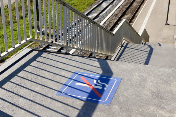 火车站。车站楼梯前有禁止吸烟的标志。背景中的栏杆和火车轨道。白天有阳光。没有人。图片下载