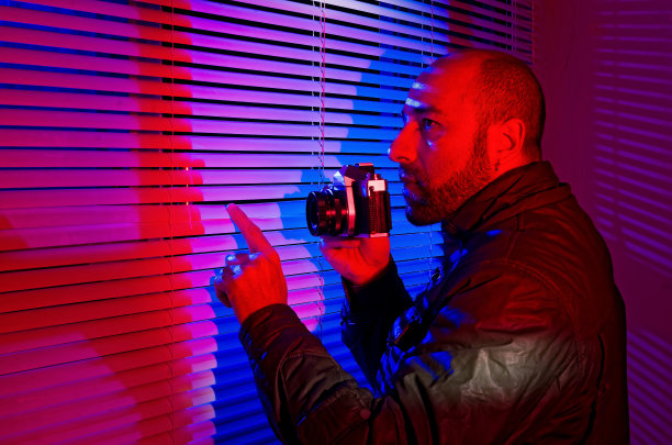 一个人拿着照相机，隔着百叶窗拍照窥探。光和颜色——红色和蓝色。图片下载