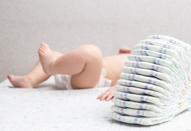 一个穿着尿布的白人小男孩躺在白色的背景上，玩着一堆尿布。文本复制空间图片下载